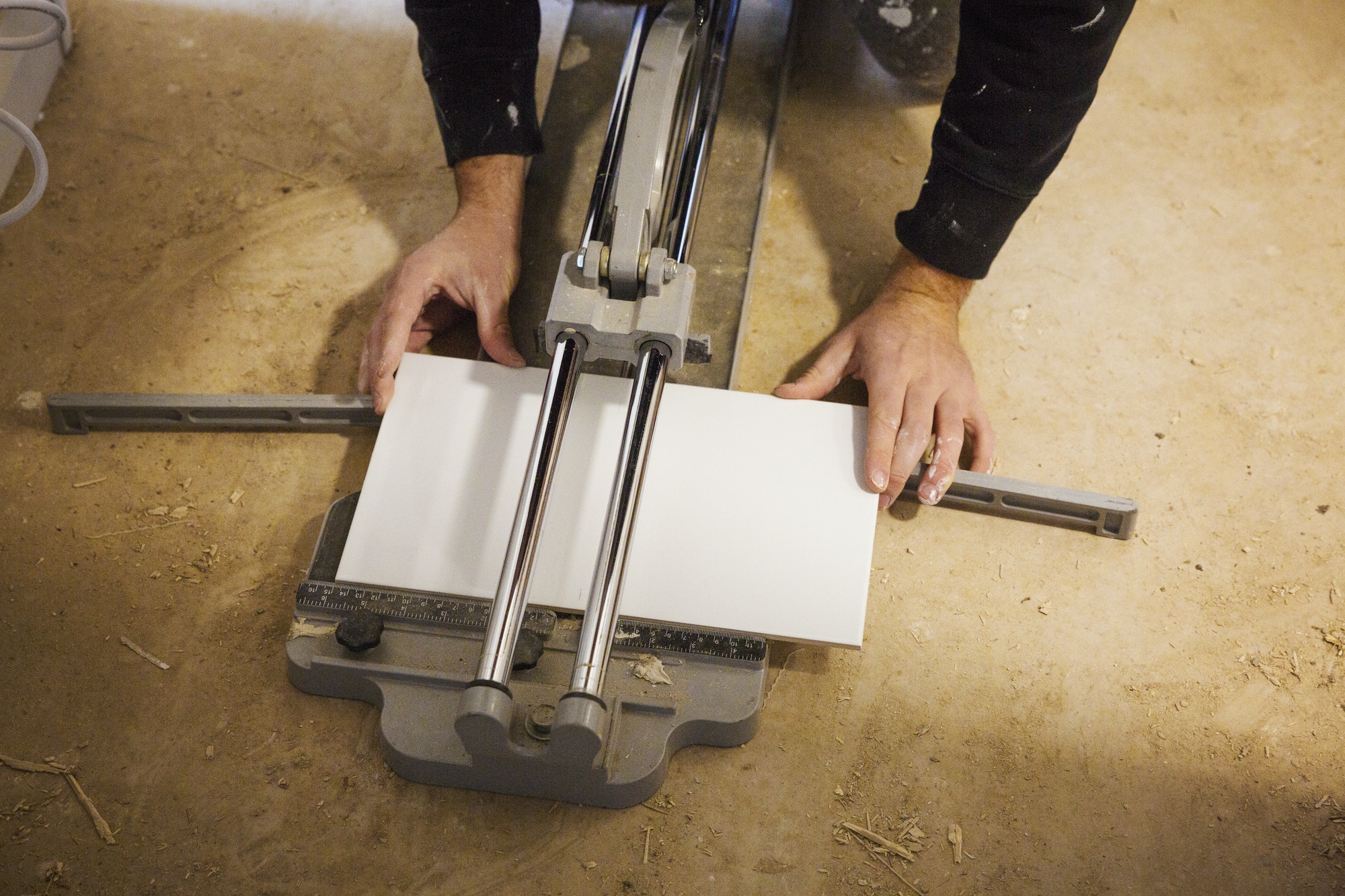 A builder, tiler kneeling on the floor, cutting a tile.